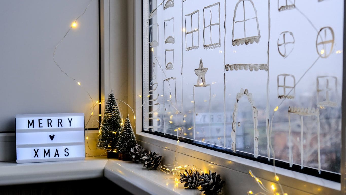Weihnachtsdeko im Büro – festlich geschmückte Fensterbank mit Lichterkette, Mini-Tannenbäumen und Weihnachtsbotschaft